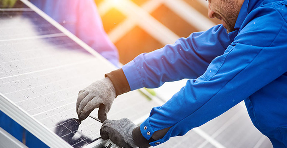 Smiling male technician in blue suit installing photovoltaic blue solar modules with screw. Man electrician panel sun sustainable resources renewable energy source alternative innovation