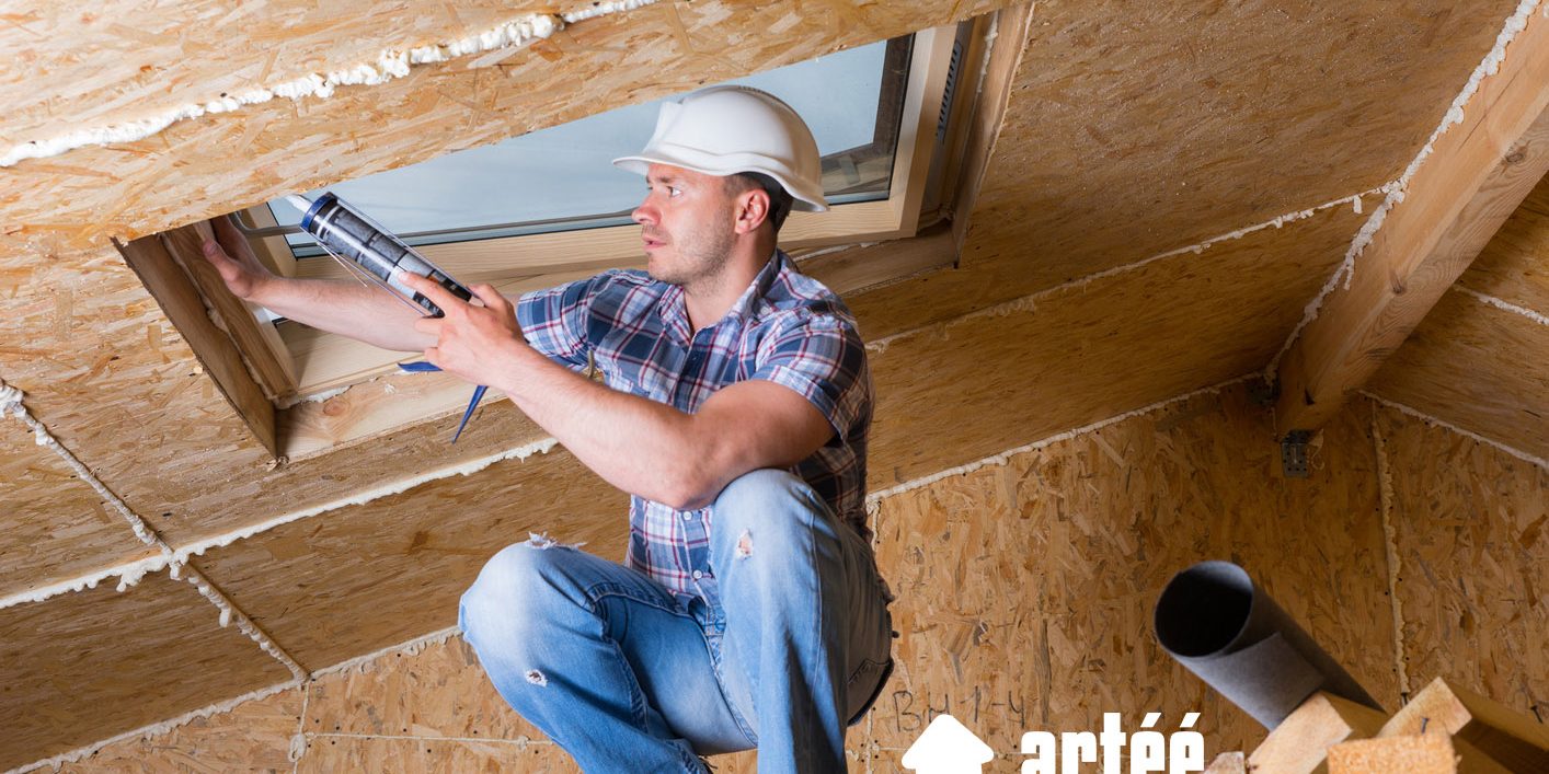 Male Construction Worker Builder Applying Fresh Caulking to Sky Light in Ceiling of Unfinished Home